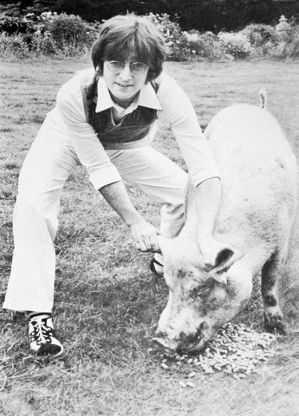 Black and white photograph of John Lennon crouching and playfully holding a pig by its ears, referencing the Beatles' 'Paul is dead' conspiracy and parodying McCartney's 'Ram' album cover.